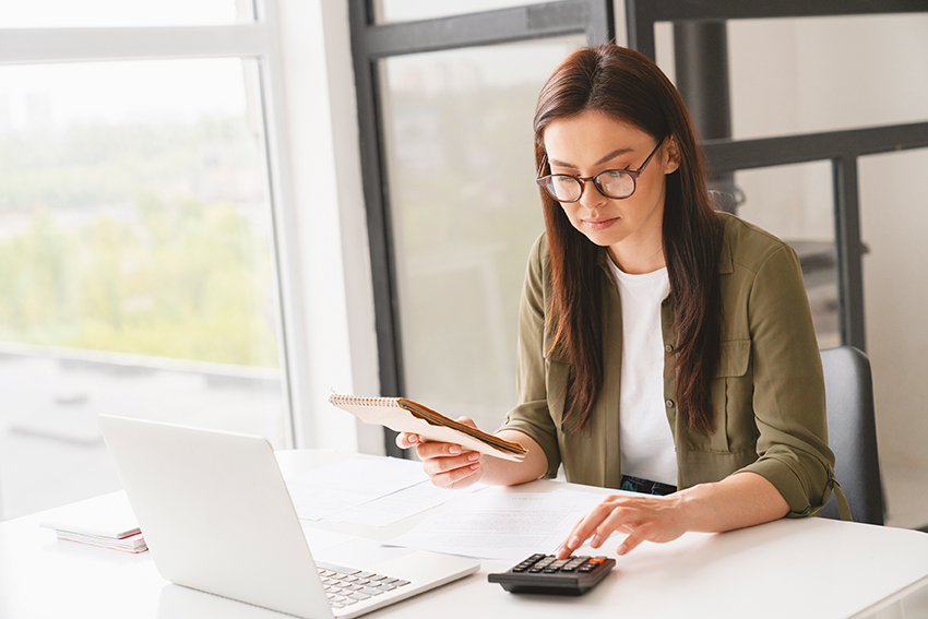 Young caucasian business woman counting funds, planning budget, paying bills online using calculator. Freelancer boss CEO doing paperwork with finances.